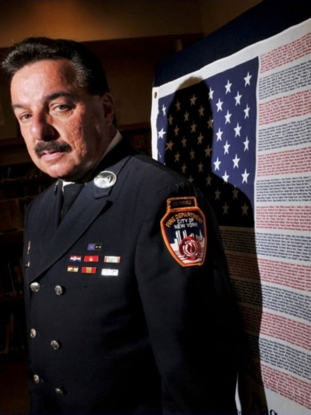 Keynote Speaker LT. Joe Torillo standing in front of a US flag with writing in its stripes